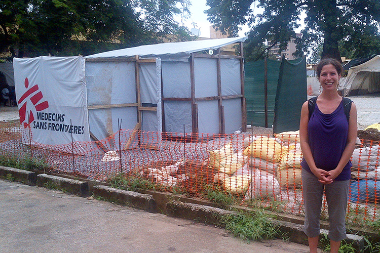 Epidemic Intelligence Service (EIS) Officer, Kelsey Mirkovic standing in front of a Médecins Sans Frontières, or Doctors without Borders banner (Guinea).
