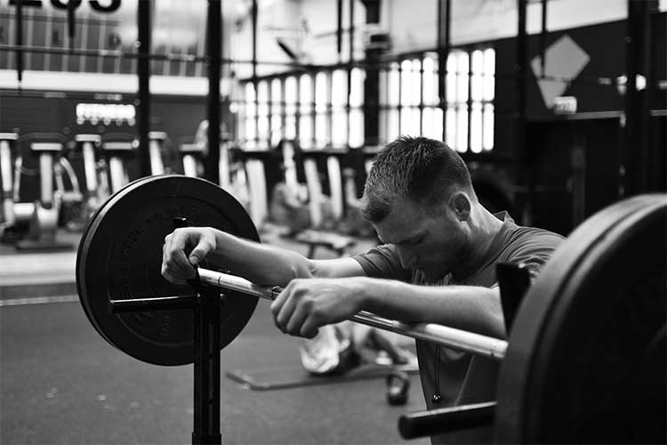 Man looking down with arms resting on a barbell whilst resting