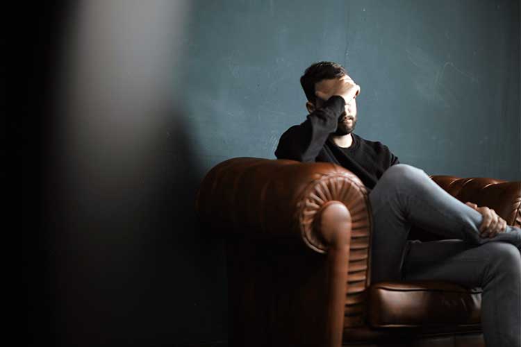 Man sitting in a chair with his hand on his face in shame